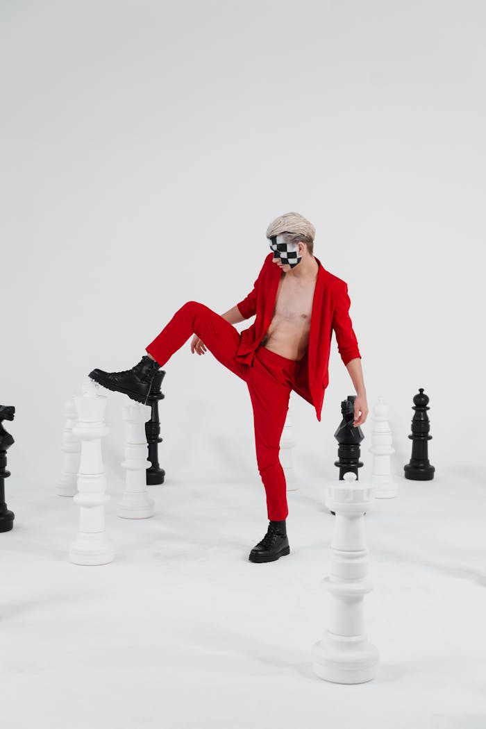 A person in red attire poses creatively with giant chess pieces, symbolizing strategy and style.